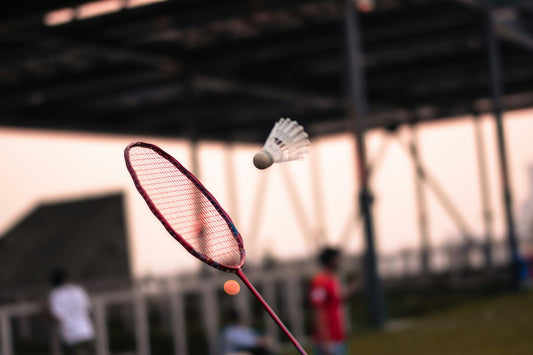 A well maintained red badminton racket hitting a shuttlecock
