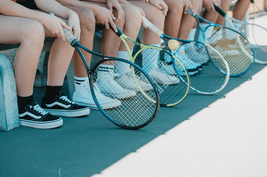 Tennis players sitting on a bench showing off their tennis rackets