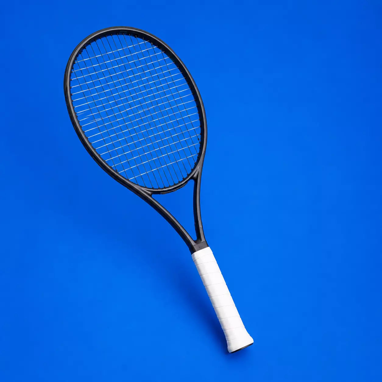 Tennis racket with hybrid restring setup showing black polyester main strings and clear multifilament cross strings on a blue background.